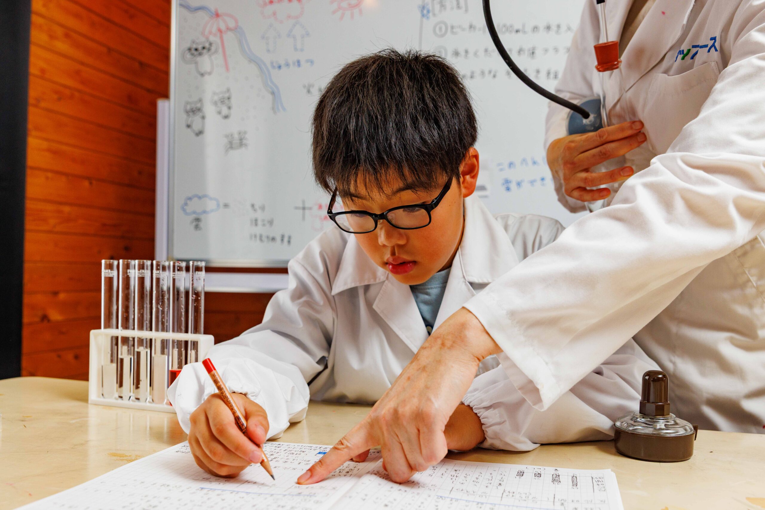 実験結果をノートにまとめる子どもを先生がサポートする様子