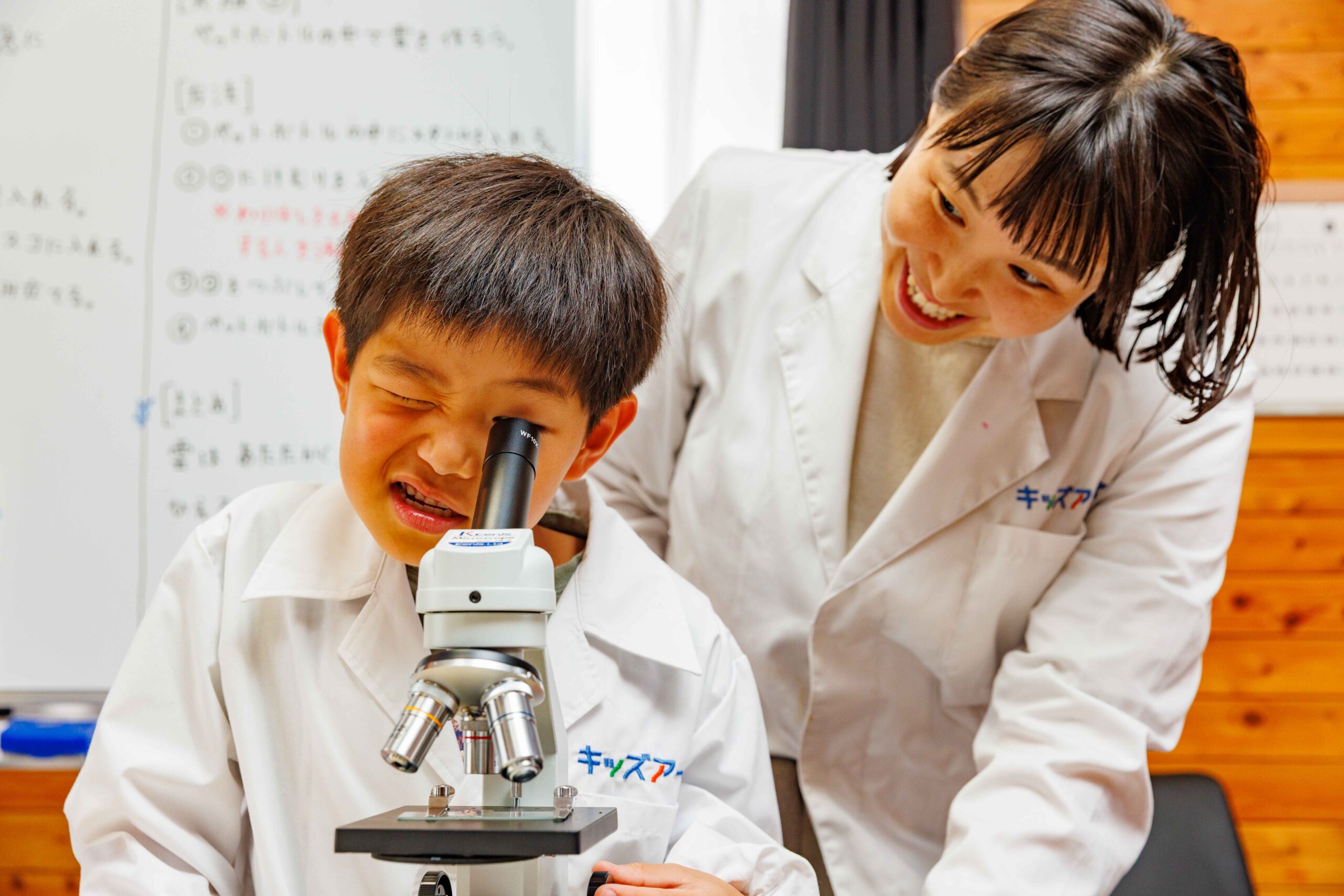 顕微鏡をのぞく子どもに寄り添う先生